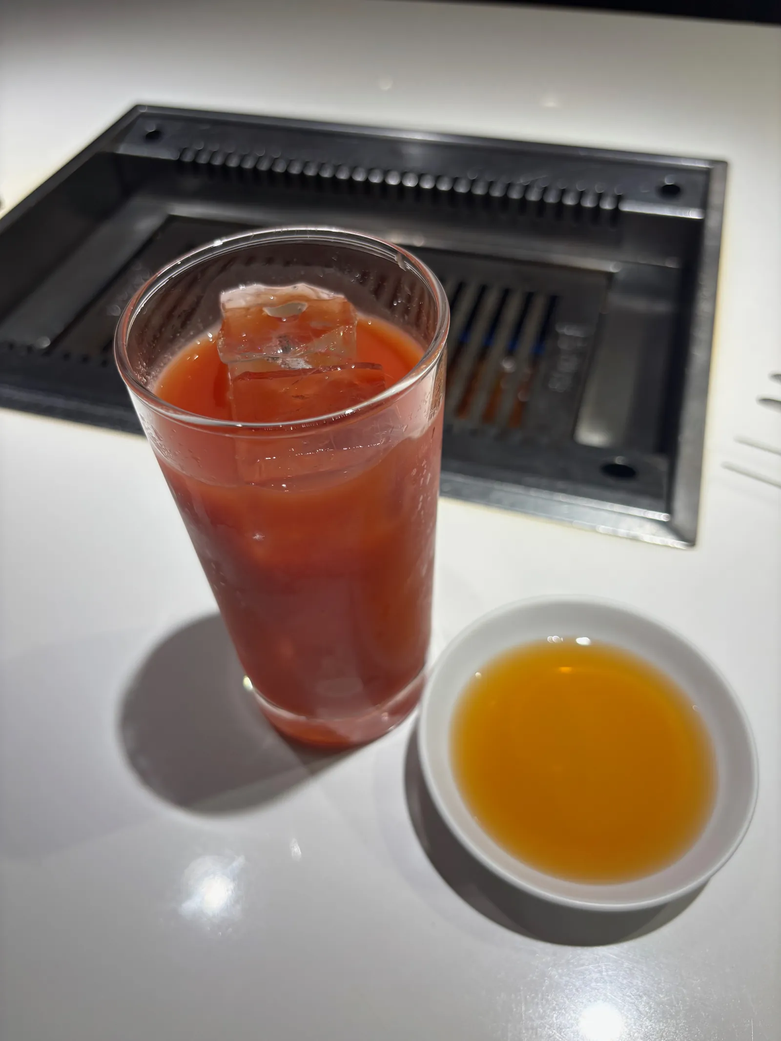 氷の入ったトマトジュースのグラス。奥にたれの入った小皿も見える