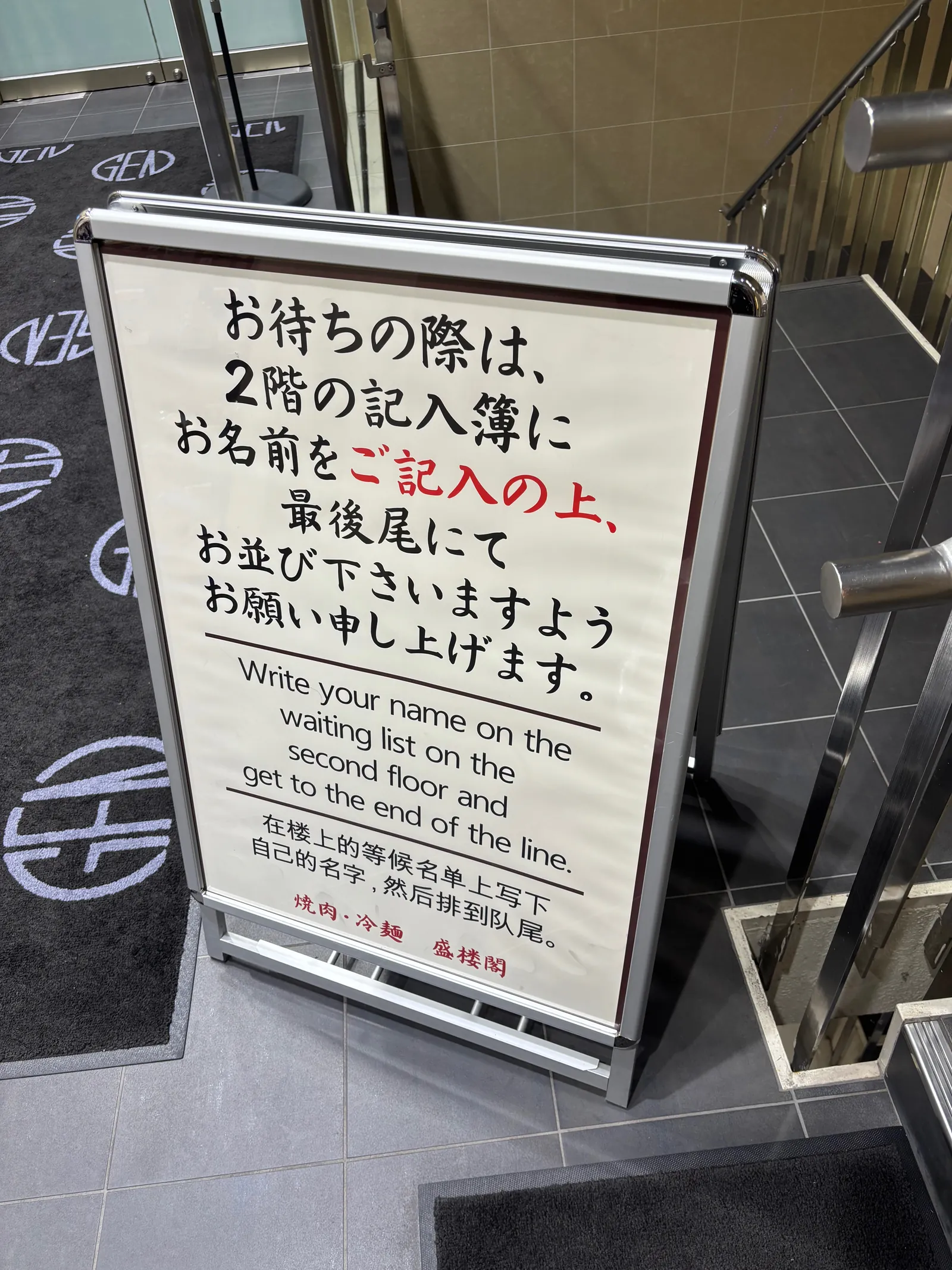「お待ちの際は、2階の記入簿にお名前をご記入の上、最後尾にてお並びくださいますようお願い申し上げます」と書かれた案内板