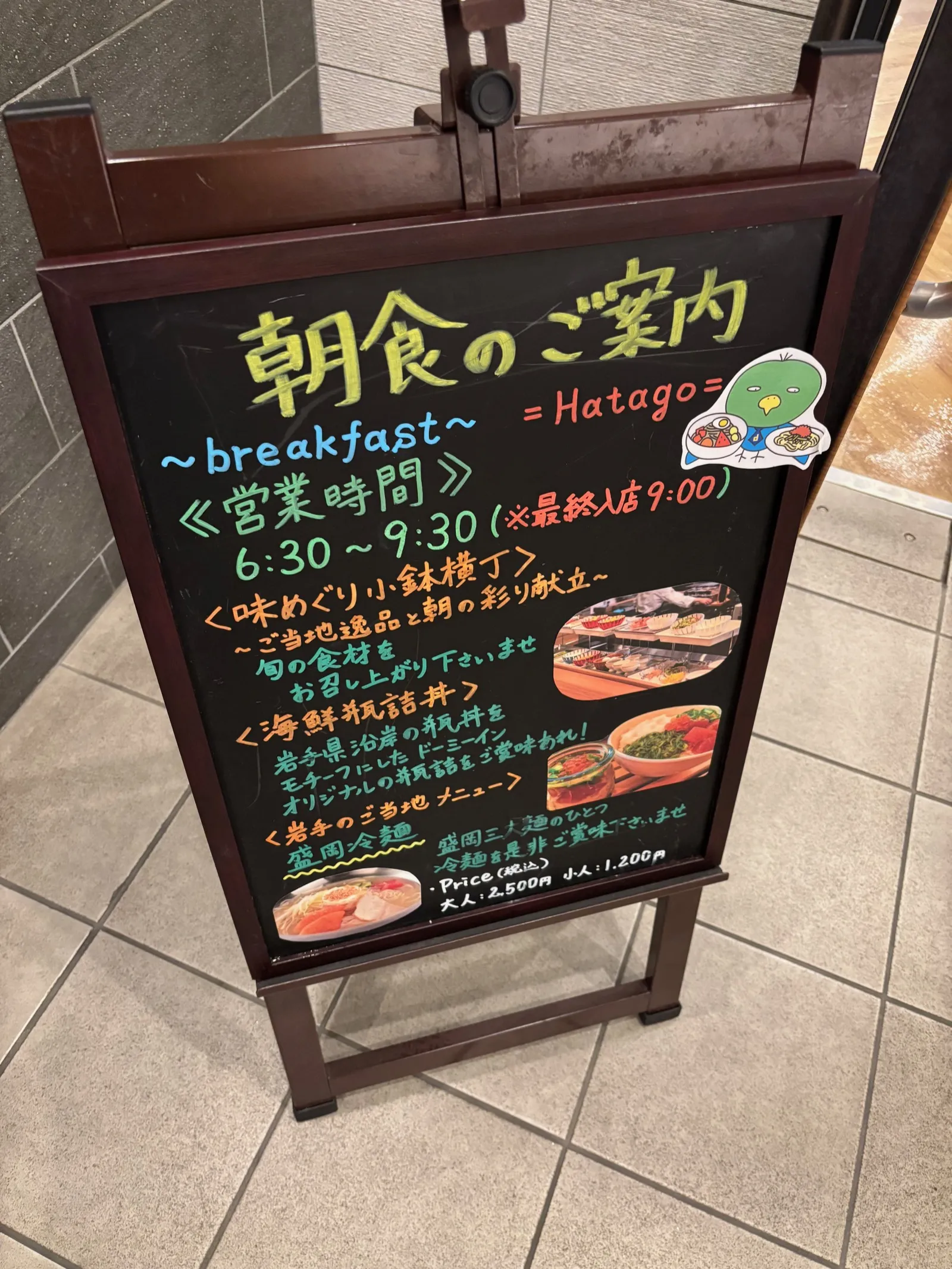 「朝食のご案内」と書かれた黒板看板。営業時間6:30〜9:30(最終入店9:00)、味めぐり小鉢横丁・海鮮瓶詰丼・盛岡冷麺の紹介と価格が書かれている