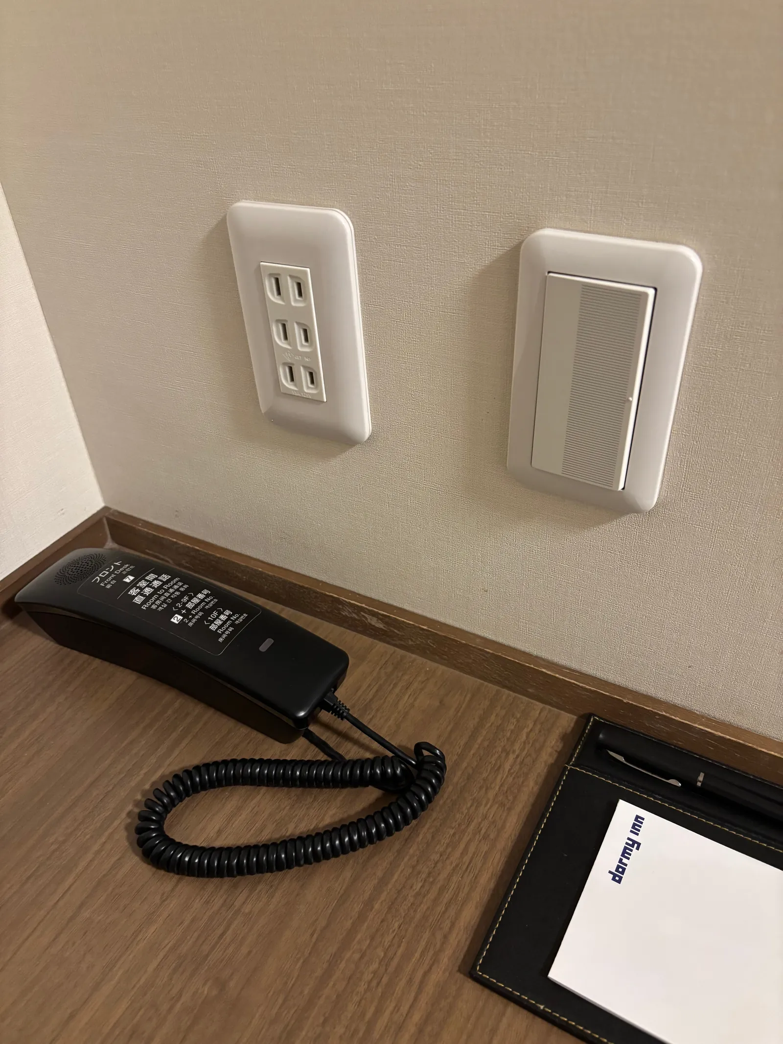 客室デスク下の壁にあるコンセント2口とスイッチ、備え付けの電話機