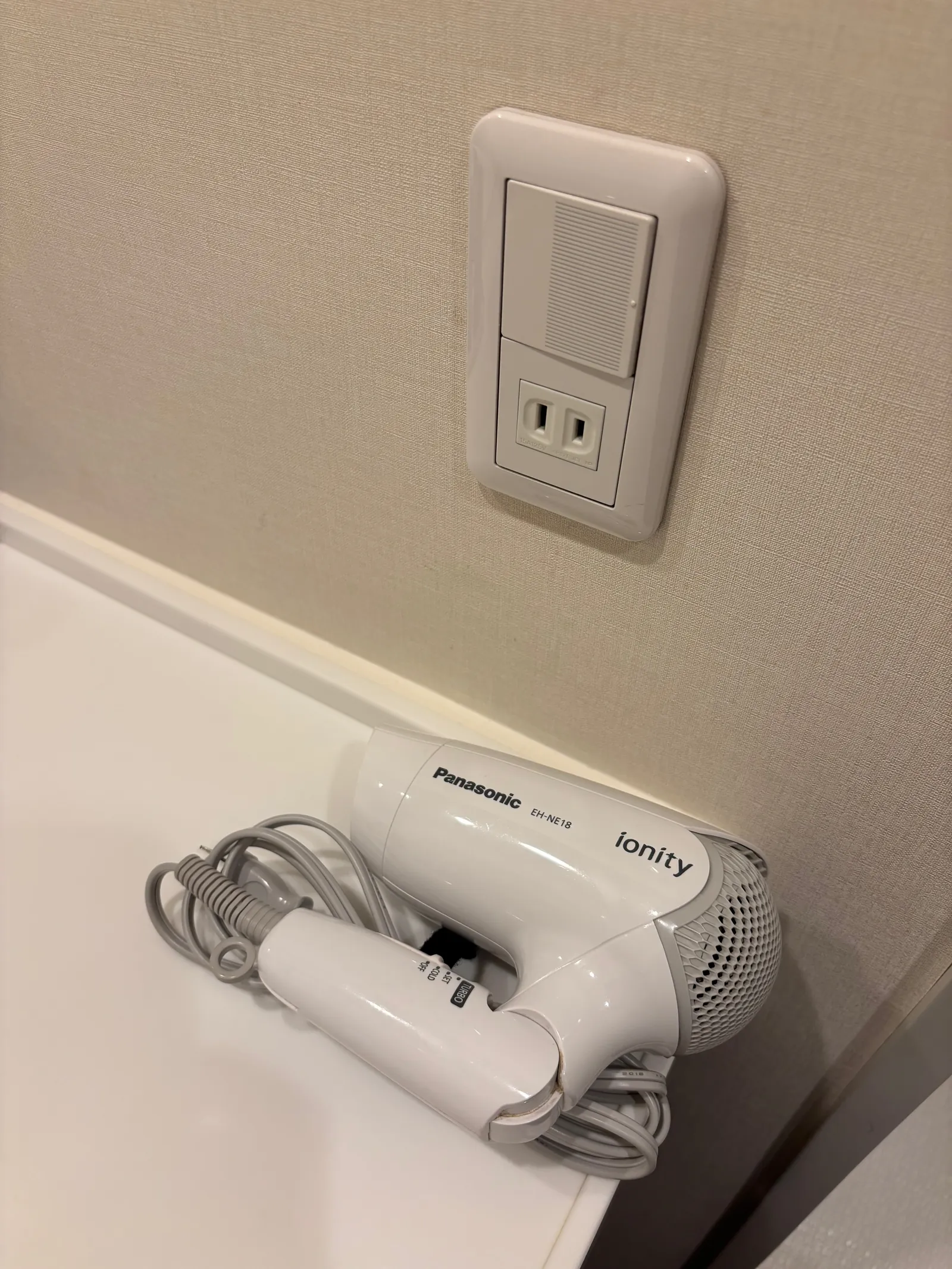 洗面台横の壁にあるコンセントと、置かれたヘアドライヤー